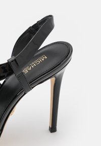 Sandale noire à talon haut avec fine bride à la cheville, semelle intérieure rembourrée et logo Michael Kors doré sur la semelle.
