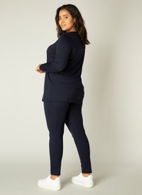 Een marineblauwe tuniek met lange mouwen gecombineerd met bijpassende nauwsluitende leggings. Zacht materiaal met een gladde textuur. Witte sneakers maken de outfit compleet.