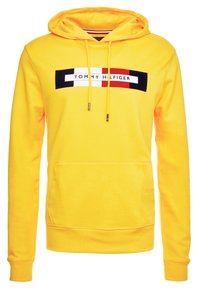 Sudadera amarilla brillante con bolsillo frontal, capucha con cordón y un logotipo rectangular de Tommy Hilfiger en negro, blanco, rojo y blanco en el pecho.