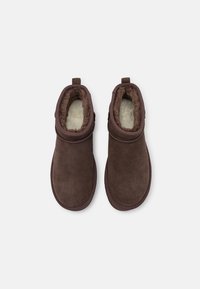 Paire de bottines marron en daim à enfiler avec une doublure intérieure en fourrure blanche et douce, vues de dessus sur un fond neutre.