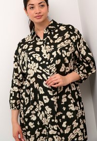 Hedvábná košile s květinovým vzorem v černé a krémové barvě, s knoflíkovým zapínáním, límcem a rukávy do tří čtvrtin; lehký materiál a volný střih.