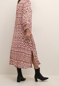 Long pink and white patterned dress with a slit, paired with black ankle boots. The fabric has a smooth texture and a flowing design.