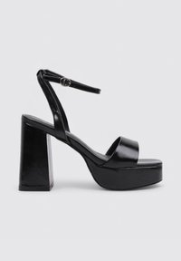 Sandalias de plataforma negras con tacón grueso, textura de cuero suave y una sola tira que cruza los dedos y rodea el tobillo.