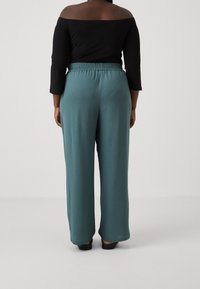 Teal vida byxorna med resårmidja, tillsammans med en svart off-shoulder topp. Slät, mjuk tyg med en avslappnad passform.