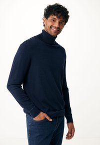Marineblauer Rollkragenpullover im figurbetonten Design, aus weichem Strickstoff mit langen Ärmeln und geripptem Kragen und Saum. Kombiniert mit Jeans.