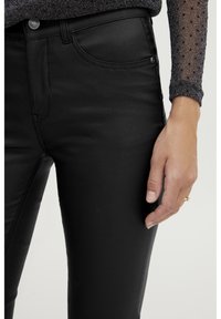 Jean noirs ajustés en tissu lisse et extensible avec un design classique à cinq poches et une fermeture à bouton métallique.