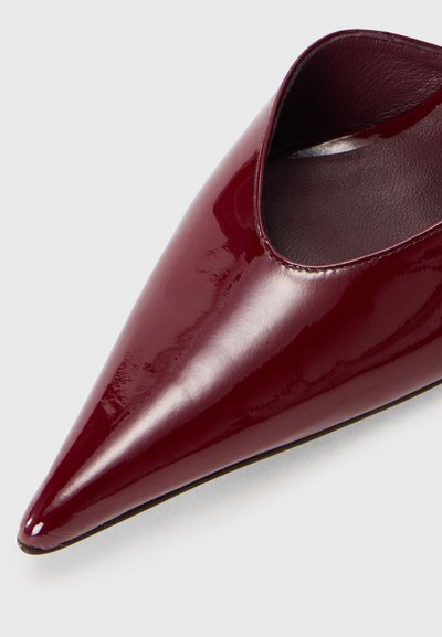 Burgundy patent leather pointed-toe shoe with an open side, smooth texture, and thin sole, showcasing a sleek, modern design.