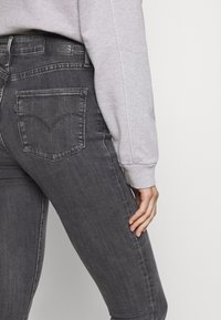 Jeans ajustados grises con un acabado desgastado, que presentan un diseño clásico de bolsillo trasero y una etiqueta de cuero en la cinturilla. Tejido de denim texturizado.