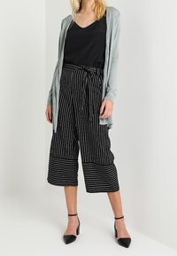 Světle šedý cardigan přes černé tílko, doplněný černobílými pruhovanými kalhotami culottes a černými lodičkami s špičatou špičkou.
