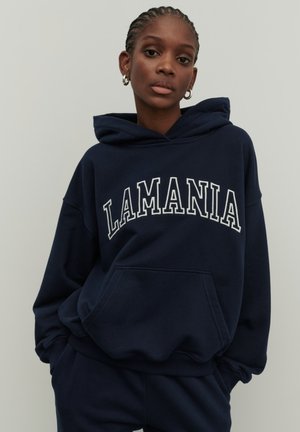 Granatowy sweatshirt z kapturem, z napisem "LAMANIA" w białych, łukowatych literach. Wykonany z miękkiego materiału, posiada przednią kieszeń i ściągacz u dołu.