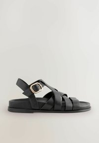 Sandales en cuir noir avec plusieurs brides croisées, une semelle plate et une fermeture à boucle latérale avec des accents dorés.