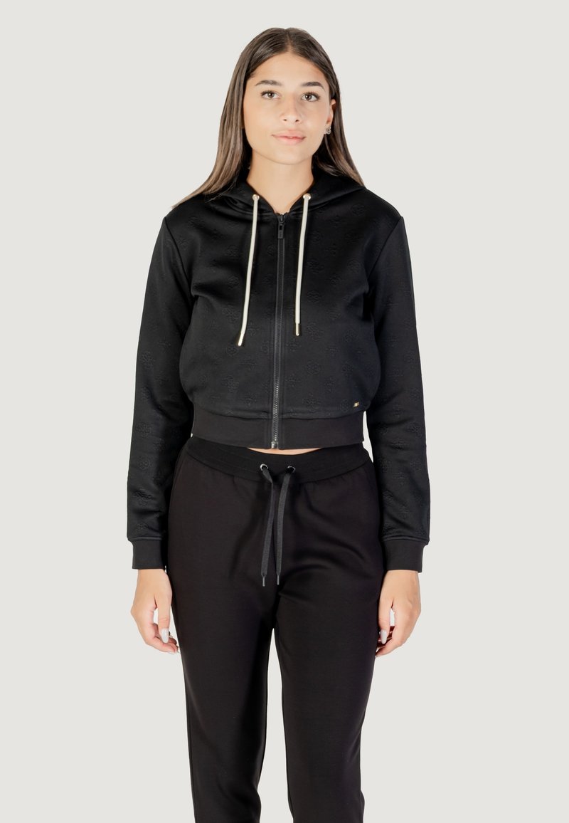 Felpa nera corta con zip frontale, cappuccio e cordini crema. Presenta un tessuto testurizzato e polsini a coste. Abbinata a pantaloni della tuta neri.