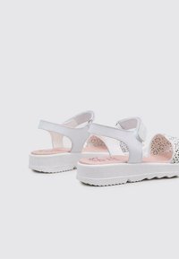 Zapatos de sandalias blancas con una suela de plataforma texturizada, correas ajustables y un diseño perforado en el lado exterior, con una plantilla rosa.