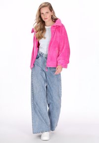 Pehmeä kirkkaan pinkki vetoketjullinen takki, rento istuvuus ja korkea kaulus. Yhdistetty vaaleansinisiin leveälahkeisiin farkkuihin ja valkoisiin lenkkareihin.