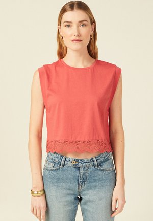 Top corto corallo realizzato in morbido cotone, con scollatura rotonda e bordo in pizzo all'orlo. Abbinato a jeans chiari in denim.