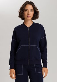 Marineblauwe ritsjack in zachte stof met een ronde halslijn, voorzakken en contrasterende stikseldetails, ontworpen voor comfort en gemak.