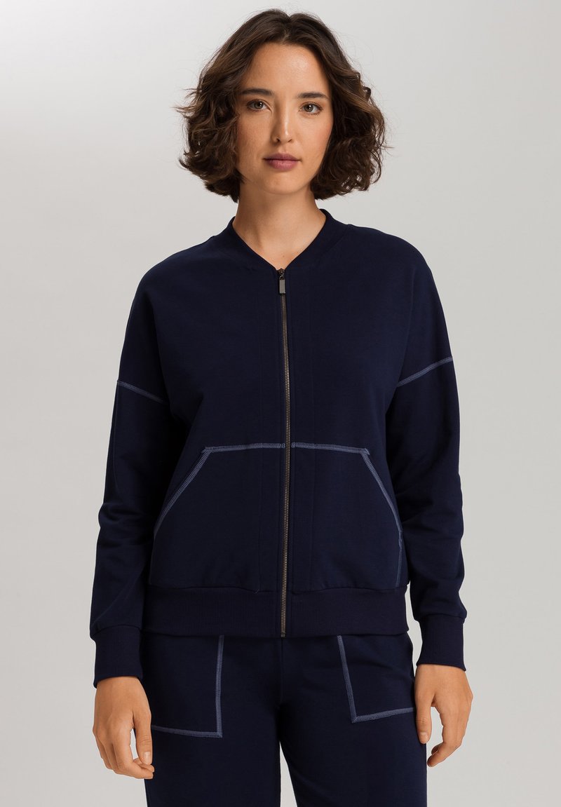Marineblauwe ritsjack in zachte stof met een ronde halslijn, voorzakken en contrasterende stikseldetails, ontworpen voor comfort en gemak.