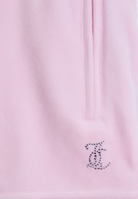 Ροζ υφασμάτινο με κάθετη ραφή και μικρό σχέδιο από στρας που σχηματίζει το στυλιζαρισμένο γράμμα «T» κοντά στο κάτω δεξί μέρος.