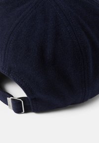 Navy blue wool cap with a curved visor, featuring visible stitching and a metal buckle adjustment at the back for size fitting.