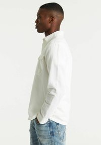 Witte blouse met lange mouwen, een button-down kraag, een enkele borstzak en zichtbaar stikwerk, gecombineerd met blauwe spijkerbroeken.