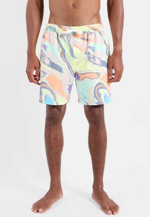 Homme portant un short de bain à motifs abstraits de couleurs pastel, avec une taille élastique et un cordon blanc, debout pieds nus sur fond blanc.