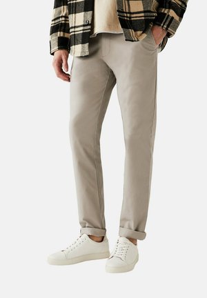 Lysegrå tapered bukser lavet af blødt stof, med sidelommer, diskret syning og oprullede nederkanter, parret med hvide sneakers.