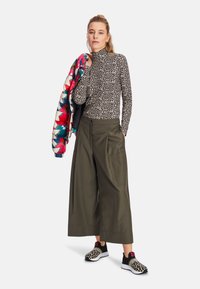 Leopard-print turtleneck, olive wide-leg pants, and multi-colored puffer jacket. Black sneakers with leopard accents.