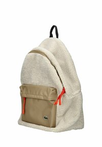 Krémový batoh vyrobený z měkké, texturované látky s hnědou přední kapsou. Obsahuje oranžové zipové táhla a černou závěsnou smyčku.