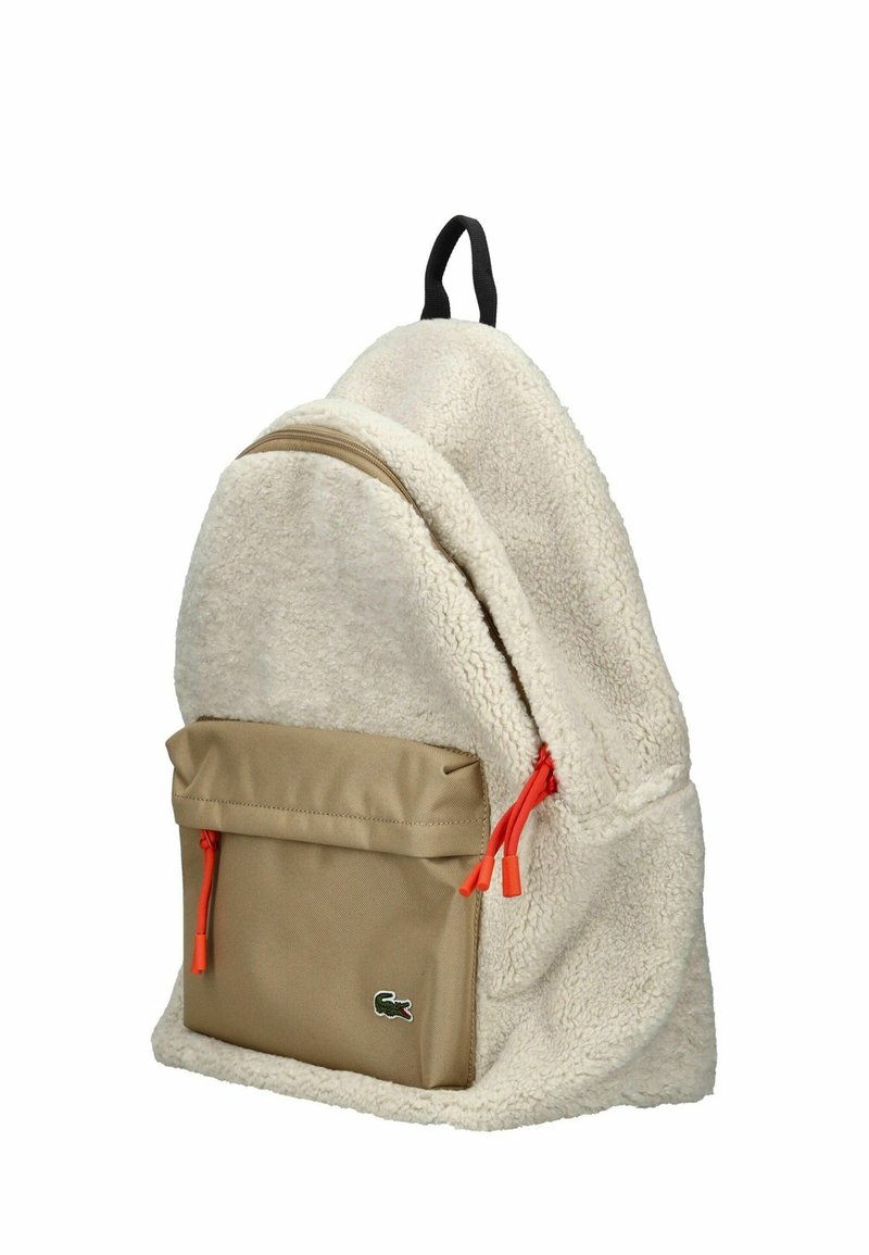 Mochila color crema hecha de un tejido suave y texturizado con un bolsillo frontal marrón. Presenta tiradores de cremallera naranja y un lazo negro para colgar.