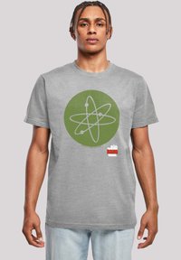 Camiseta de algodón gris con un gráfico circular verde que presenta un diseño de átomo. Incluye acentos en rojo y blanco en la parte inferior. Mangas cortas.
