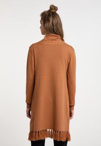 Lange, roestkleurige cardigan met een hoge kraag, geribbelde details en een franjerand. Gemaakt van zacht brei-materiaal met zijzakken.