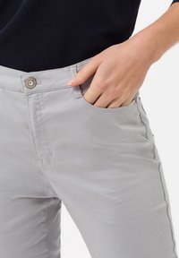 Pantalons gris clair avec une coupe slim, dotés d'une poche avant, d'un détail piqué et d'une fermeture à bouton au niveau de la taille. Texture de tissu lisse.