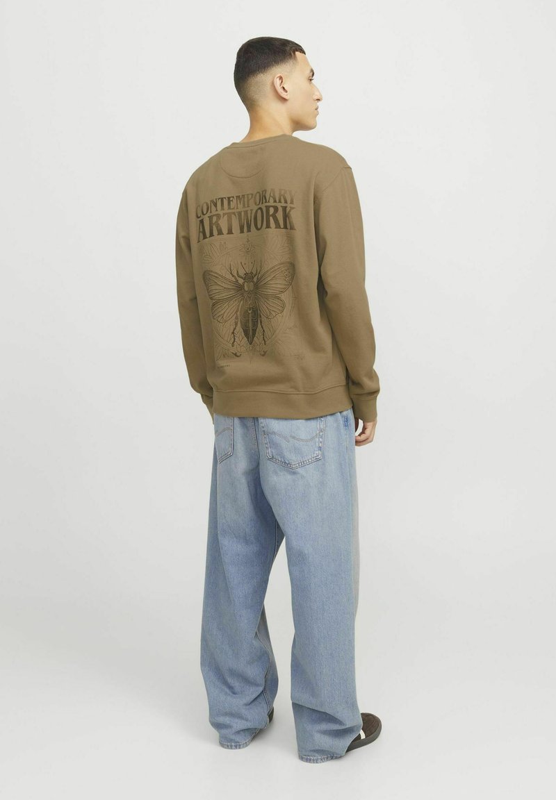 Sudadera marrón con un gran gráfico negro de una polilla y las palabras "ARTWORK CONTEMPORÁNEO" en la parte de atrás. Pantalones de denim azul de corte holgado.