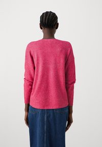 Suéter de punto fucsia con mangas largas, que presenta un escote redondeado y un corte relajado. Combinado con una falda de mezclilla oscura.