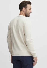 Beige kötött pulóver bordázott mandzsettával és aljjal. Puha tapintású, laza szabású, kerek nyakkivágással és látható minták vagy díszítések nélkül.