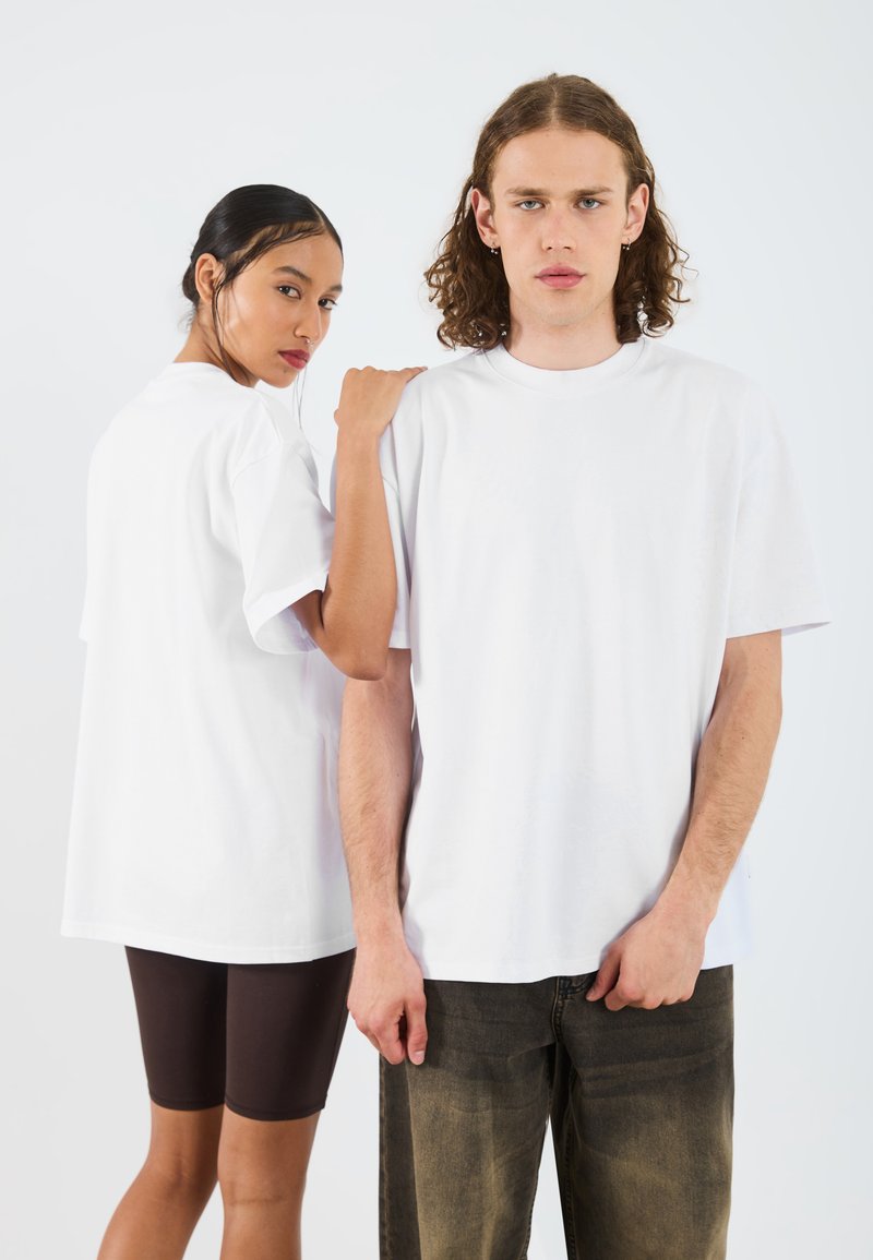 White oversized cotton t-shirts on two people; one shown from front, the other from back. Featured with loose sleeves and a crew neckline.