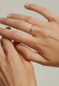 Anillo en tono dorado con un diseño ondulado que presenta acentos alternos planos y puntiagudos, llevado en una mano con uñas naturales.