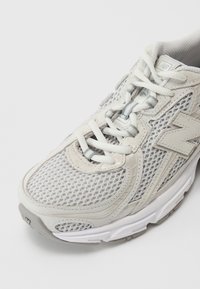 Gray mesh athletic shoe with white laces, padded collar, and a textured rubber sole. Features a large gray logo on the side.