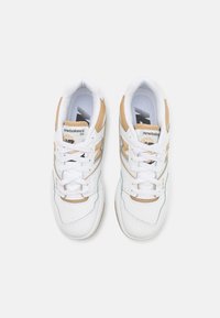 White leather sneakers with beige accents. Rounded toe, flat laces, and padded collar. Features "newbalance" logo and model number on tongue.