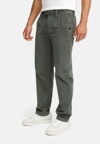 Gray corduroy trousers with pleated front, side pockets, and a fitted waist. Paired with white sneakers for a casual look.