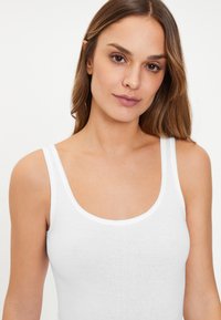 White cotton tank top with a scoop neckline and slim shoulder straps. Soft texture, form-fitting design, and no visible patterns or accents.