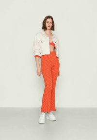 Calças flare de padrão vermelho com cintura elástica e uma jaqueta de ganga branca cropped, usadas com ténis brancos de plataforma.