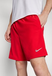 Rote Sportshorts von Nike mit einem elastischen Bund, seitlichen Taschen und einem kleinen silbernen Logo auf der linken unteren Seite. Glatte Stoffoberfläche.