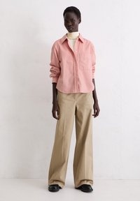 Pink button-up shirt with long sleeves, paired with beige wide-leg trousers and black shoes. Smooth textures and relaxed fit.