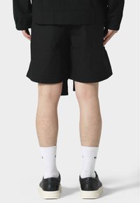 Black shorts with a relaxed fit, featuring a smooth texture. Worn with white socks and black sneakers, showing the back view of the outfit.