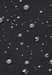 Tessuto nero con molteplici gocce d'acqua, di dimensioni variabili, che riflettono la luce; superficie liscia che evidenzia la caratteristica impermeabile.