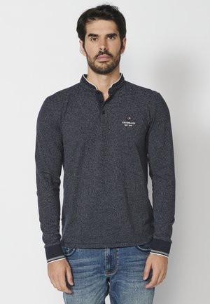 Marineblauwe katoenen longsleeve shirt met een henley-kraag, drie-knopen-lijst en witte stiksels bij de manchet en kraag. Logo op de borst.
