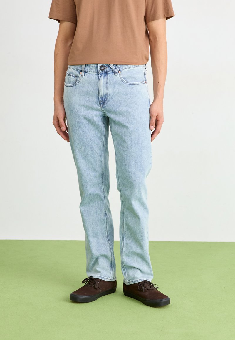 Lichtblauwe denim jeans met een rechte pijp, vijfzakkenontwerp, gecombineerd met een bruine t-shirt met korte mouwen en donkere sneakers.