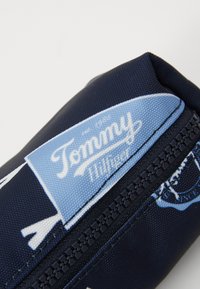 Blå tygpenna med dragkedja, prydd med en Tommy Hilfiger-logotyp, mönstrad design och en slät textur. Kompakt och cylindrisk form.