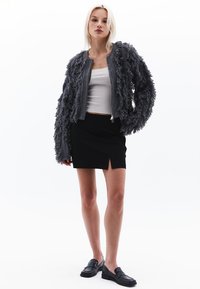 Grå texturerad bombarejacka med fransdetaljer, ihop med en svart minikjol med slits fram. Svarta loafers fulländar outfiten.